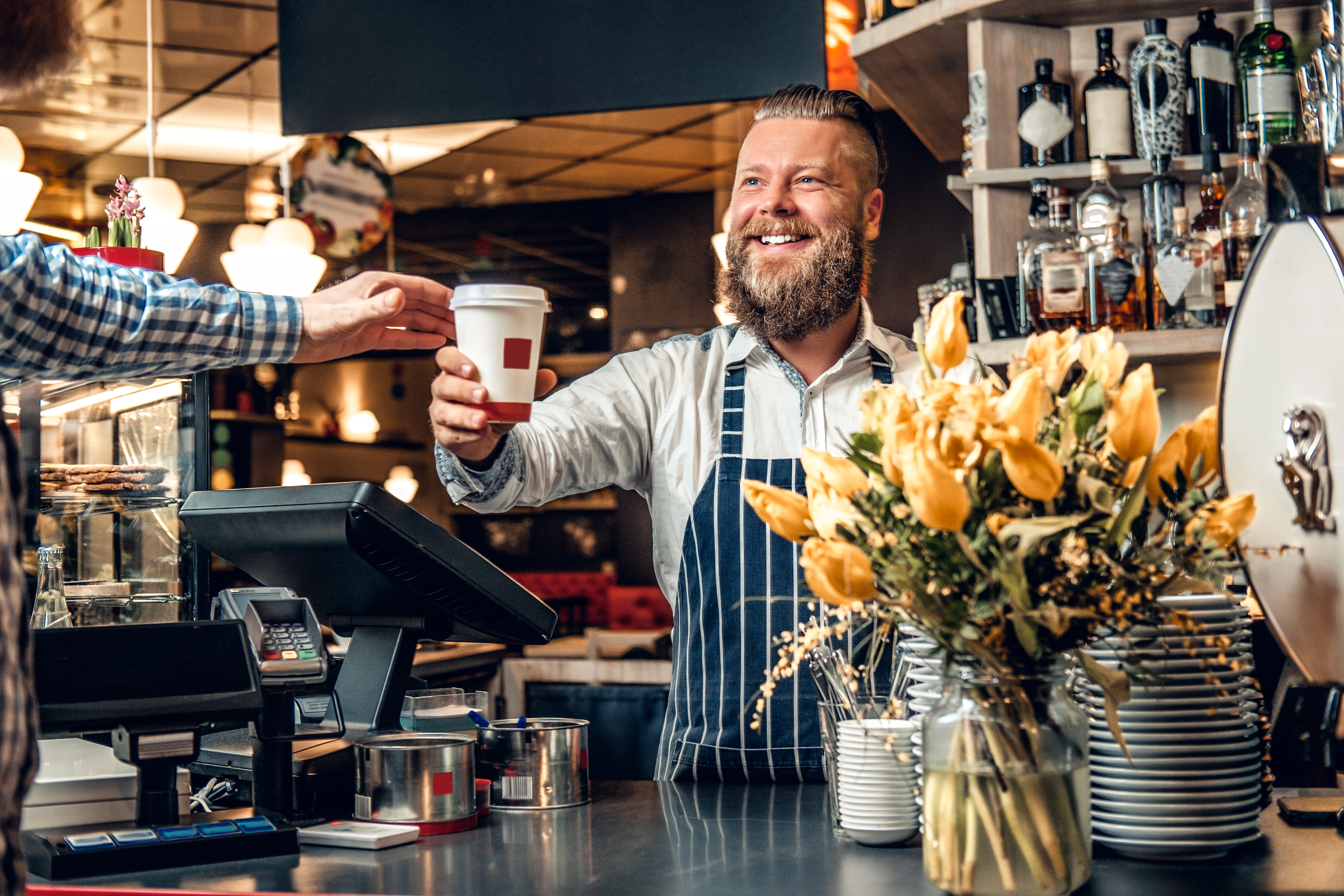 barista in coffee shop handing coffee over pos system