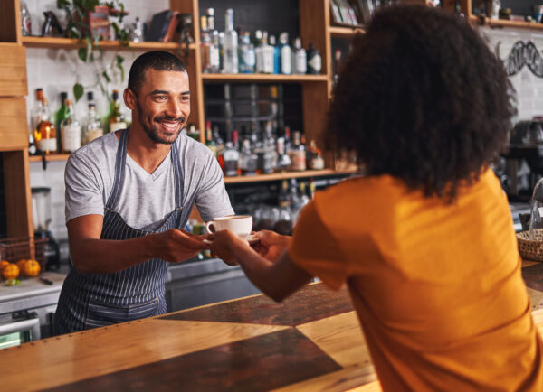 Male barista serves coffee cup to female customer in cafe Barista handing over coffee in cafe