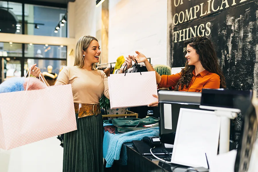 Beautiful young blond woman paying her new clothes buyed in expensive boutique with credit card.