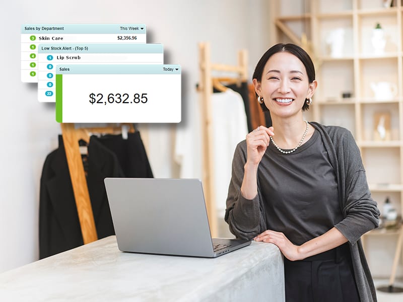 A smiling store manager stands beside a laptop displaying sales reports and analytics from a Beauty Supply POS System, showing daily revenue and product performance.