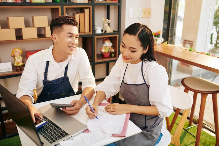 Two people in aprons looking at a computer and reports.